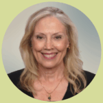 Beverley smiles brightly. She has long, wavy blonde hair and wears gold jewelry with a modest black blouse.