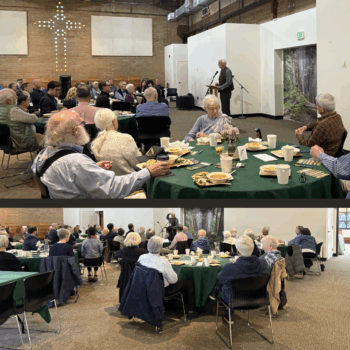 Photo of Samaritan Center Luncheon. Guests sit around round tables in a church fellowship hall. The tables are dressed in green tablecloths with elegant northwest centerpieces. Guests eat as they listen to Kurt present.