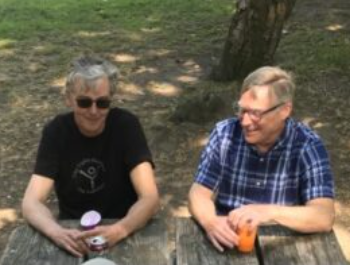 Lee Seese and Doug Farnham sit at a picnic table together and smile at the camera,