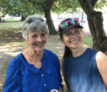 Peggy Hansen and Deb Thomas smile for the camera in front of knobby maple trees.