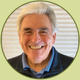 Rob smiles at the camera. He has white and silver hair combed back, and wears a blue polo shirt under a grey pullover with a zipper.